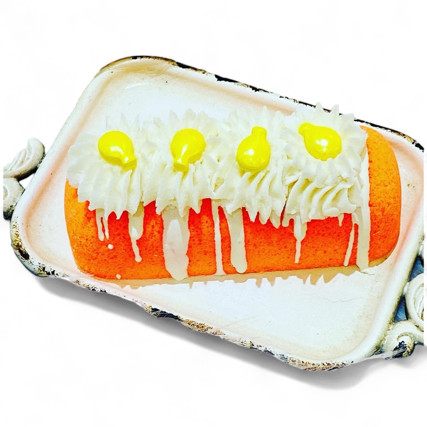 An orange twinkie bath bomb topped with white frosting and yellow sugar sprinkles on a white tray against a white background