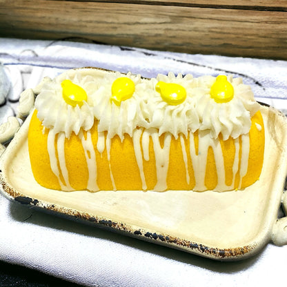 A yellow twinkie bath bomb topped with white frosting and yellow sugar sprinkles on a white tray on top of a white towel