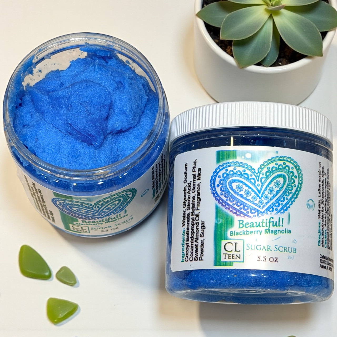Two jars of blue sugar scrub with visible brand labels on a white surface.