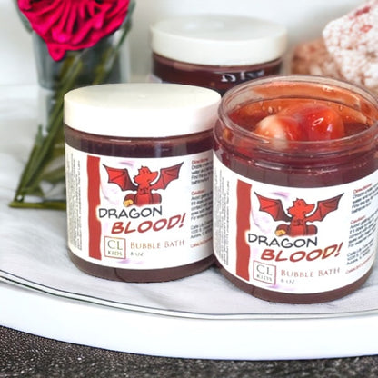 Two jars of 'Dragon Blood' bubble bath on a white surface with decorative elements.
