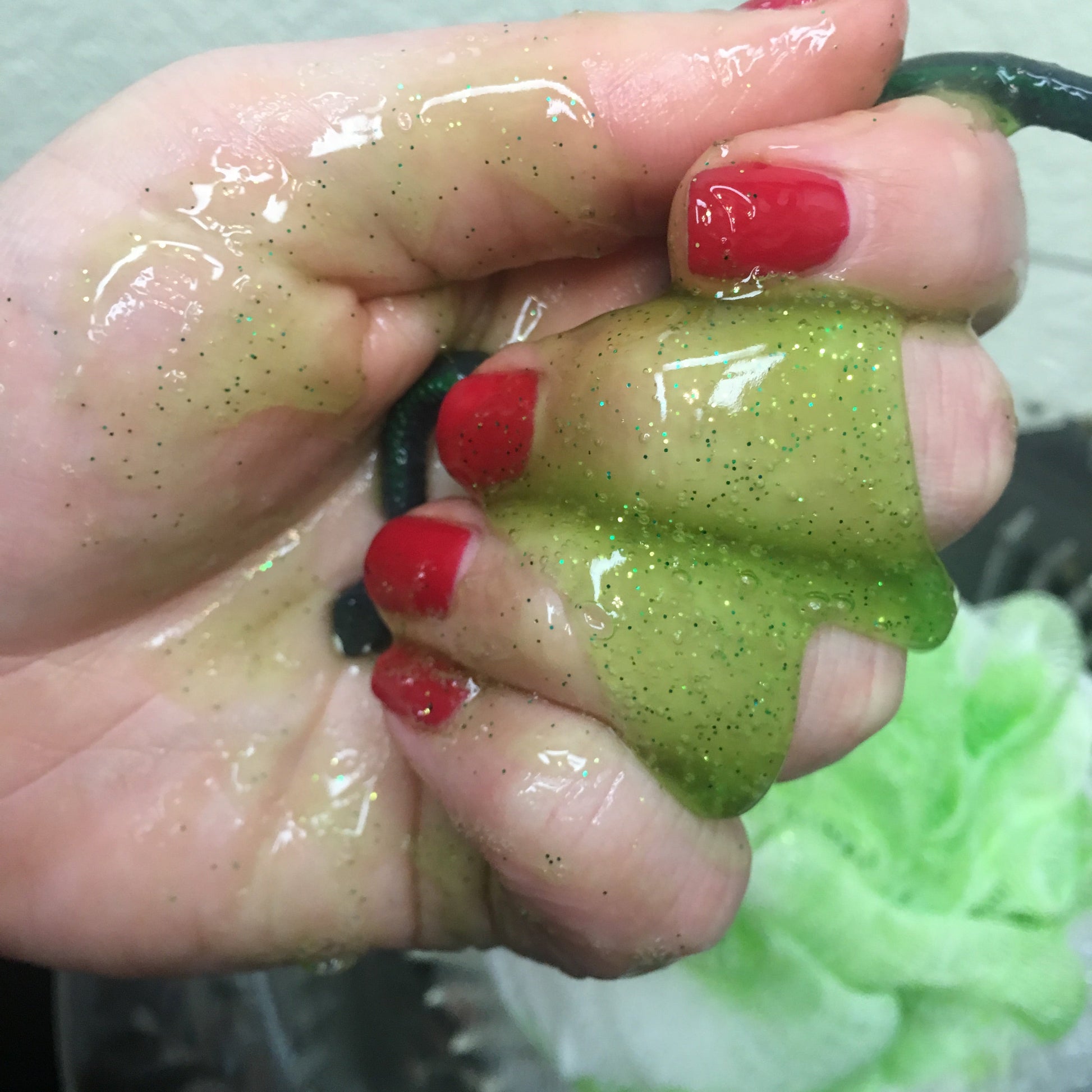 Hand holding green slime with black specks, against a blurred background