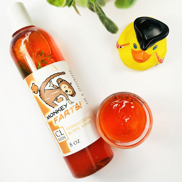 Monkey Farts Shimmering Body Wash in a transparent bottle and cup of our orange monkey farts body wash against a white background