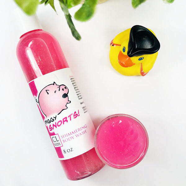 Piggy Snorts Shimmering Body Wash in a transparent bottle and cup of our pink piggy snorts body wash against a white background