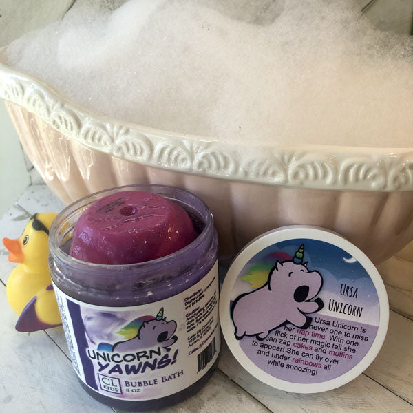 Jar of unicorn-themed bubble bath with a purple scoop and decorative container in the background.